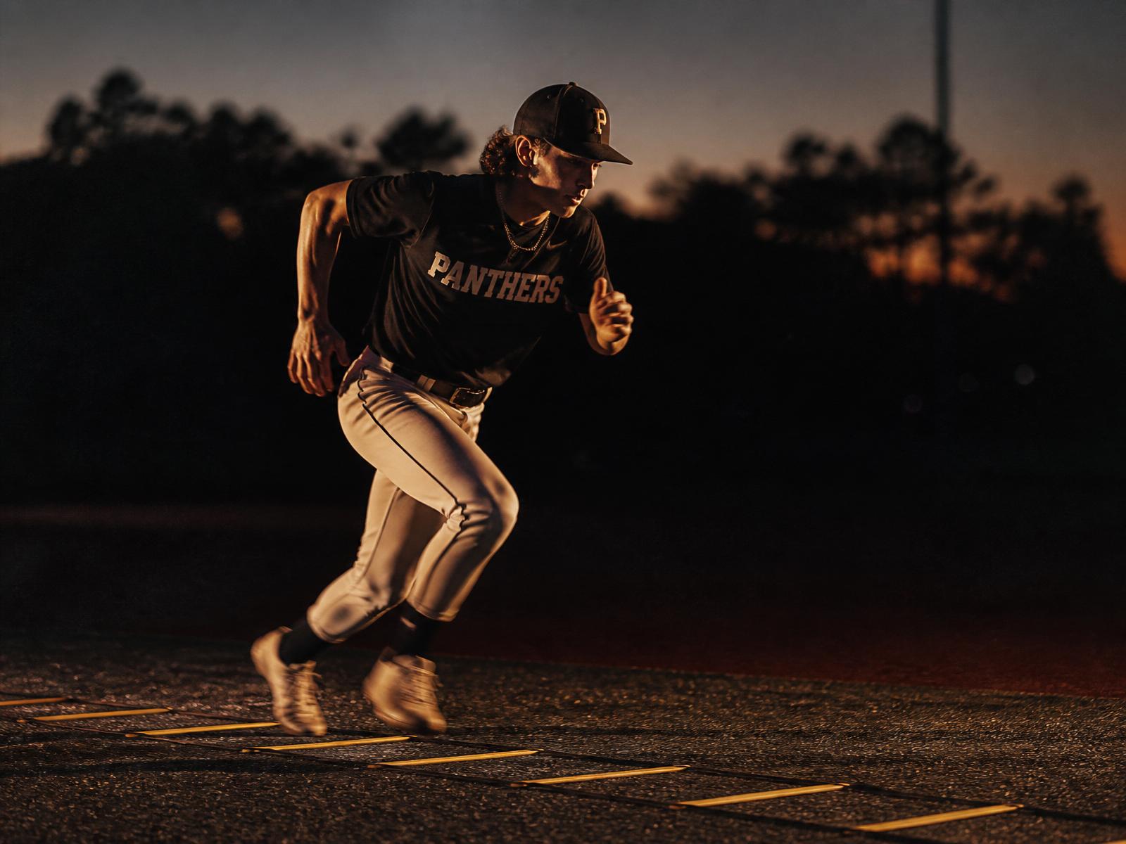 Baseball player sprinting through agility ladder at dusk